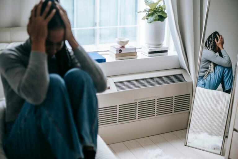 Sad young woman sitting alone in room with head in hands and knees pulled into chest.