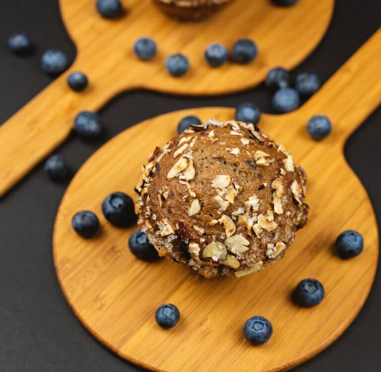 Blueberry oatmeal muffin on a round wooden board, surrounded by fresh blueberries