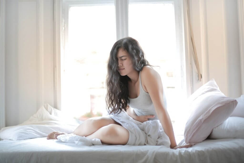 Woman sitting on bed with a stomach ache, holding belly