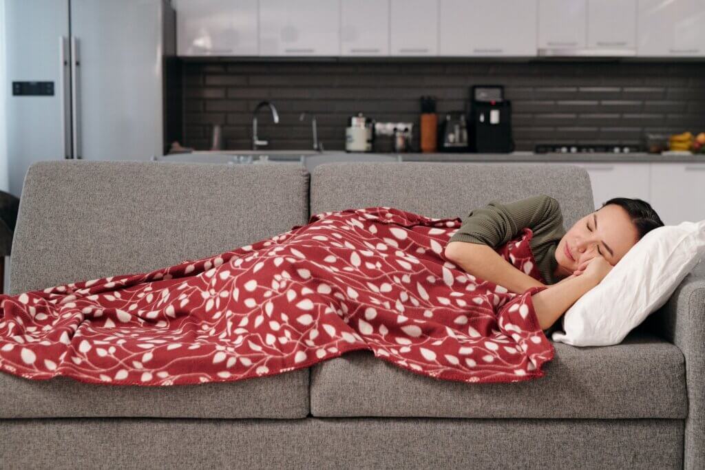 Woman sleeping on light brown sofa, covered by red blanket