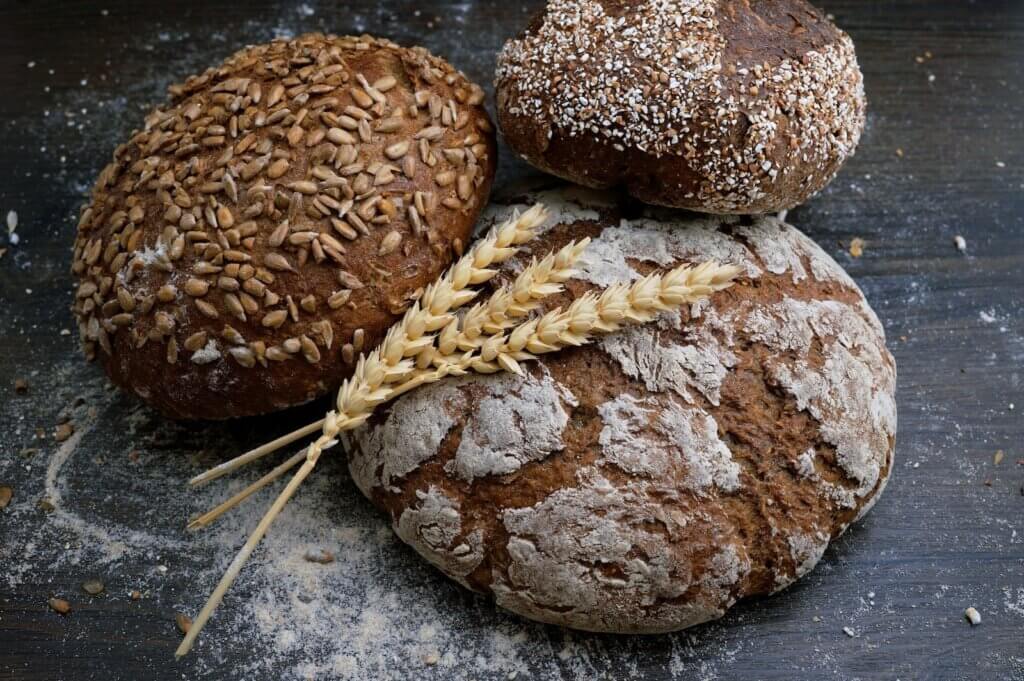 three loaves of dark wheat bread, with a stalk of wheat, on a dark background