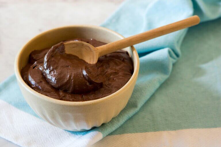 Chocolate pudding in white ceramic bowl, with wooden spoon, sitting on folded light blue fabric napkin