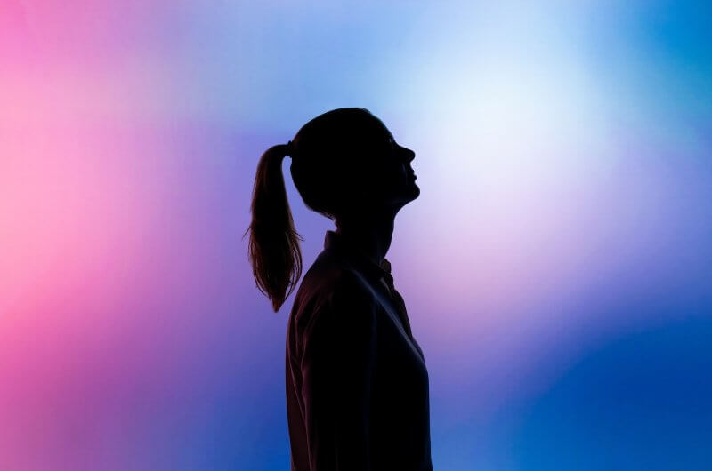 Side View Silhouette of Woman With Hair In Ponytail On A Pink and Blue Background
