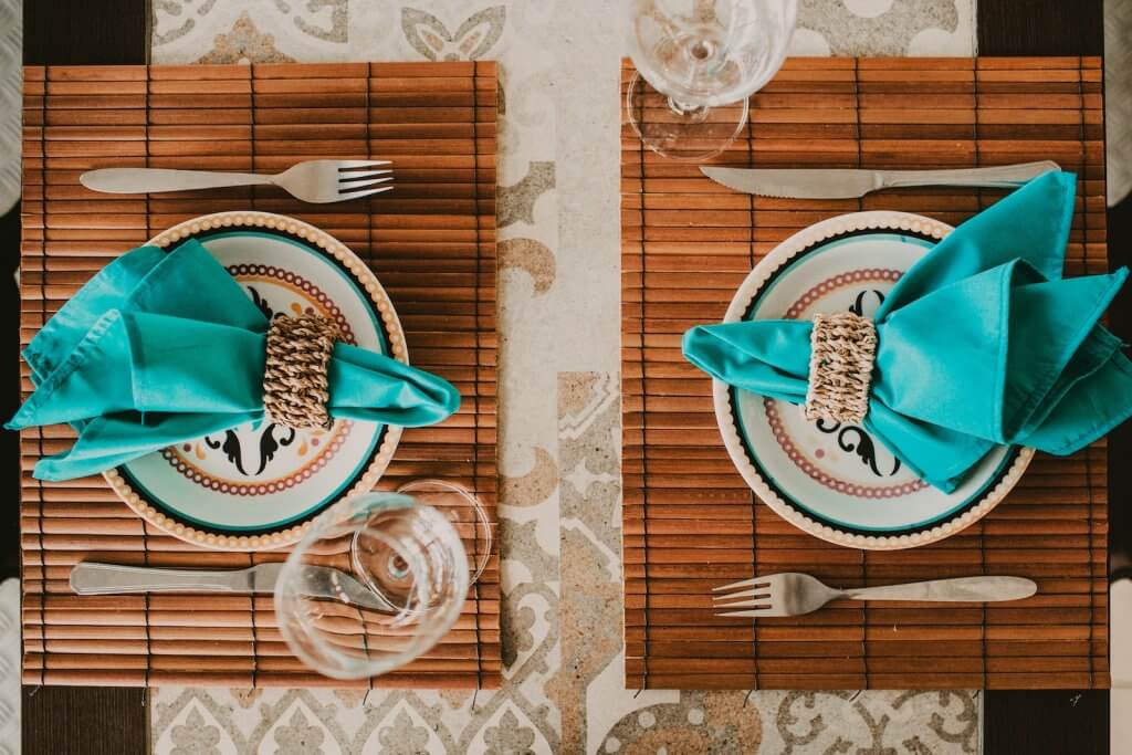 Top view stylish arrangement of ornamental plates with blue napkins served on place mat on table near wineglasses