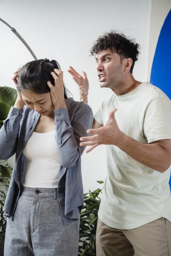 A Man in a White Shirt Shouting at his Partner, Covering Her Ears and Looking Down