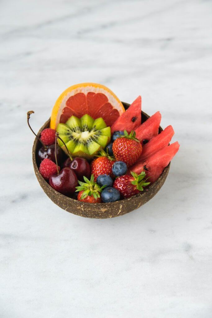 Fresh fruits cut attractively in a brown bowl on top of a white marble surface
