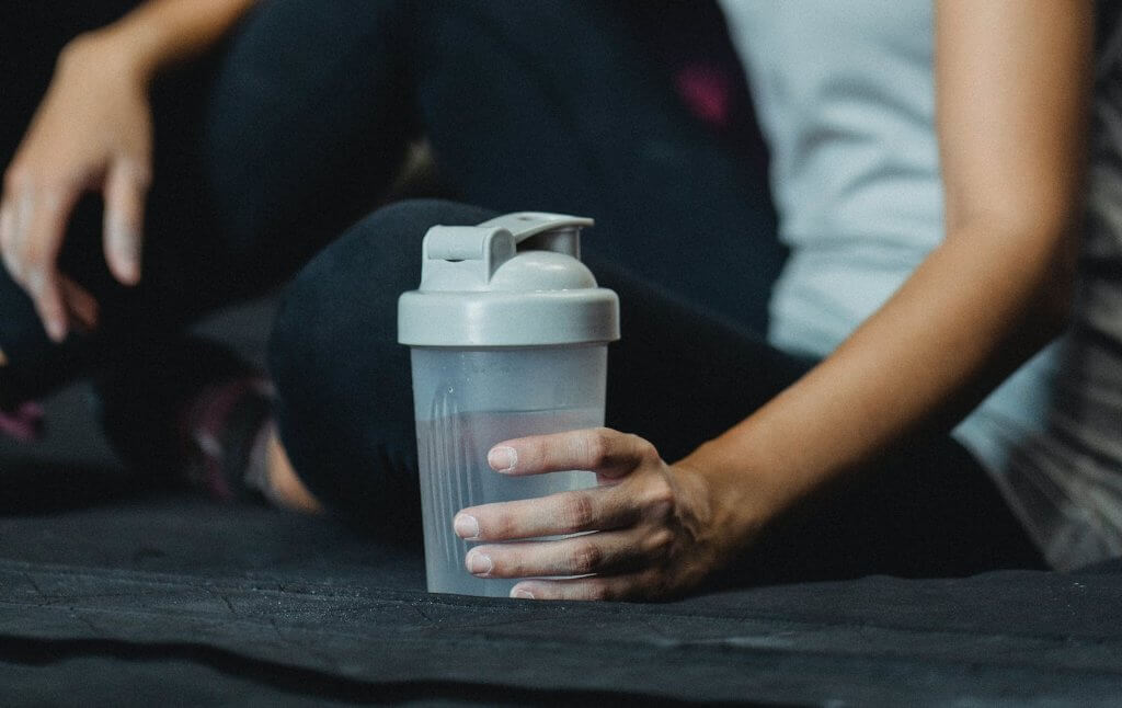 Side view crop sportswoman sitting on floor with water bottle and resting