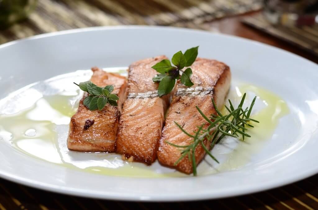 Cooked salmon fillets on a white plate with fresh herbs on top